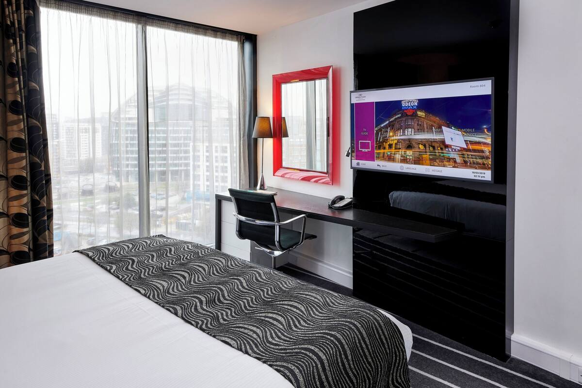 Een hotelkamer met een bed, een bureau, een stoel, een televisie en een raam met gordijnen.