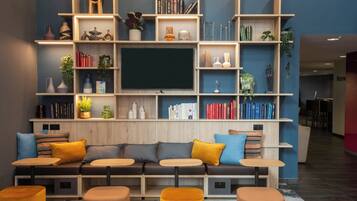 Un espace de vie moderne comprenant un canapé, des poufs, un téléviseur et des étagères remplies de livres et d’objets décoratifs.