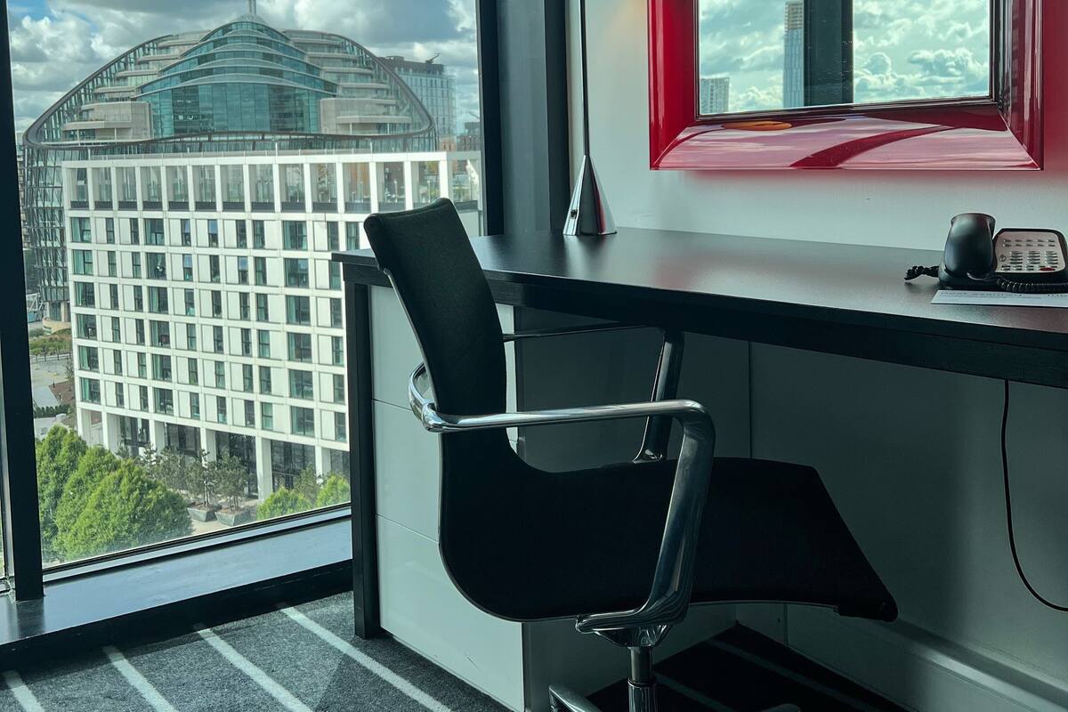 Een moderne kantoorruimte met een bureau, stoel en een raam met uitzicht op een stadsbeeld en een opvallend gebouw.