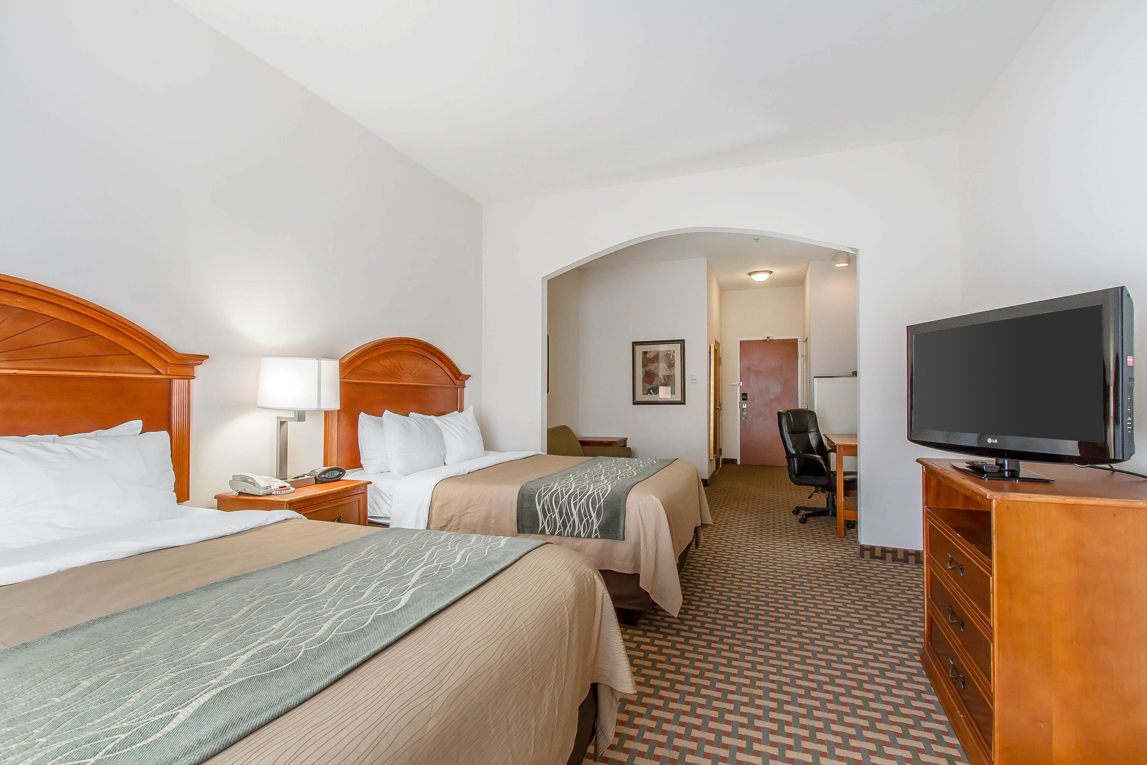 A hotel room with two beds, a TV, a desk, and a chair.