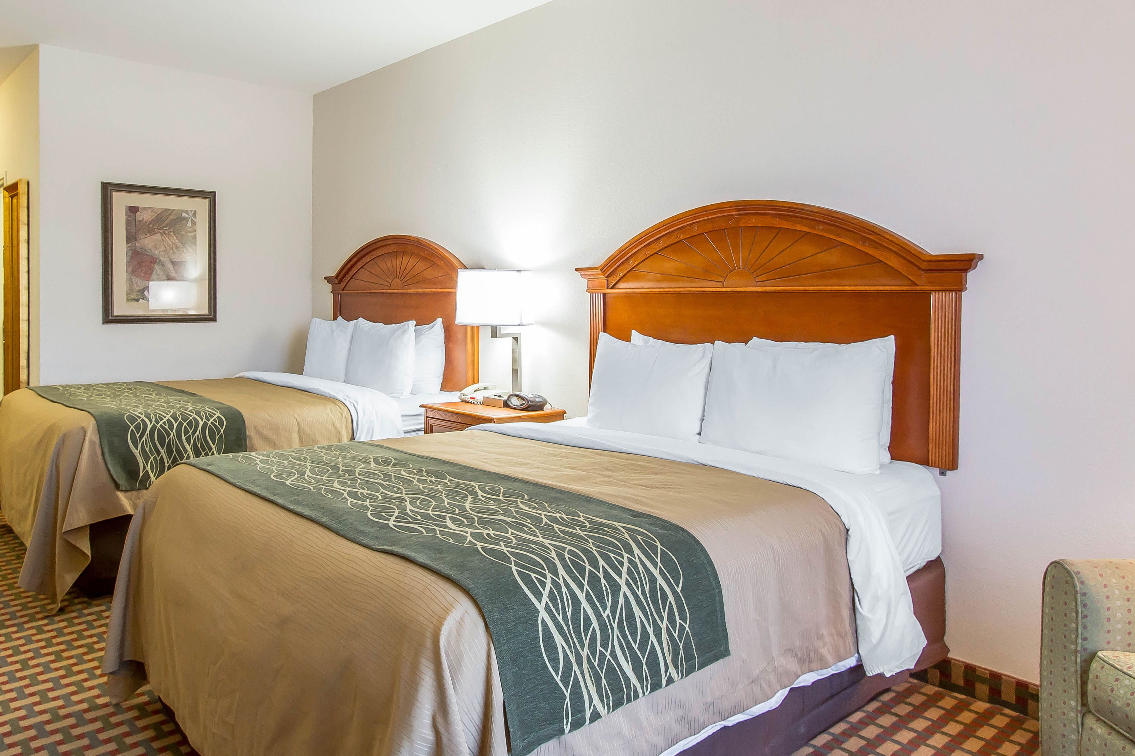 A hotel room with two beds, each with a wooden headboard, a nightstand, a lamp, and a framed picture on the wall.