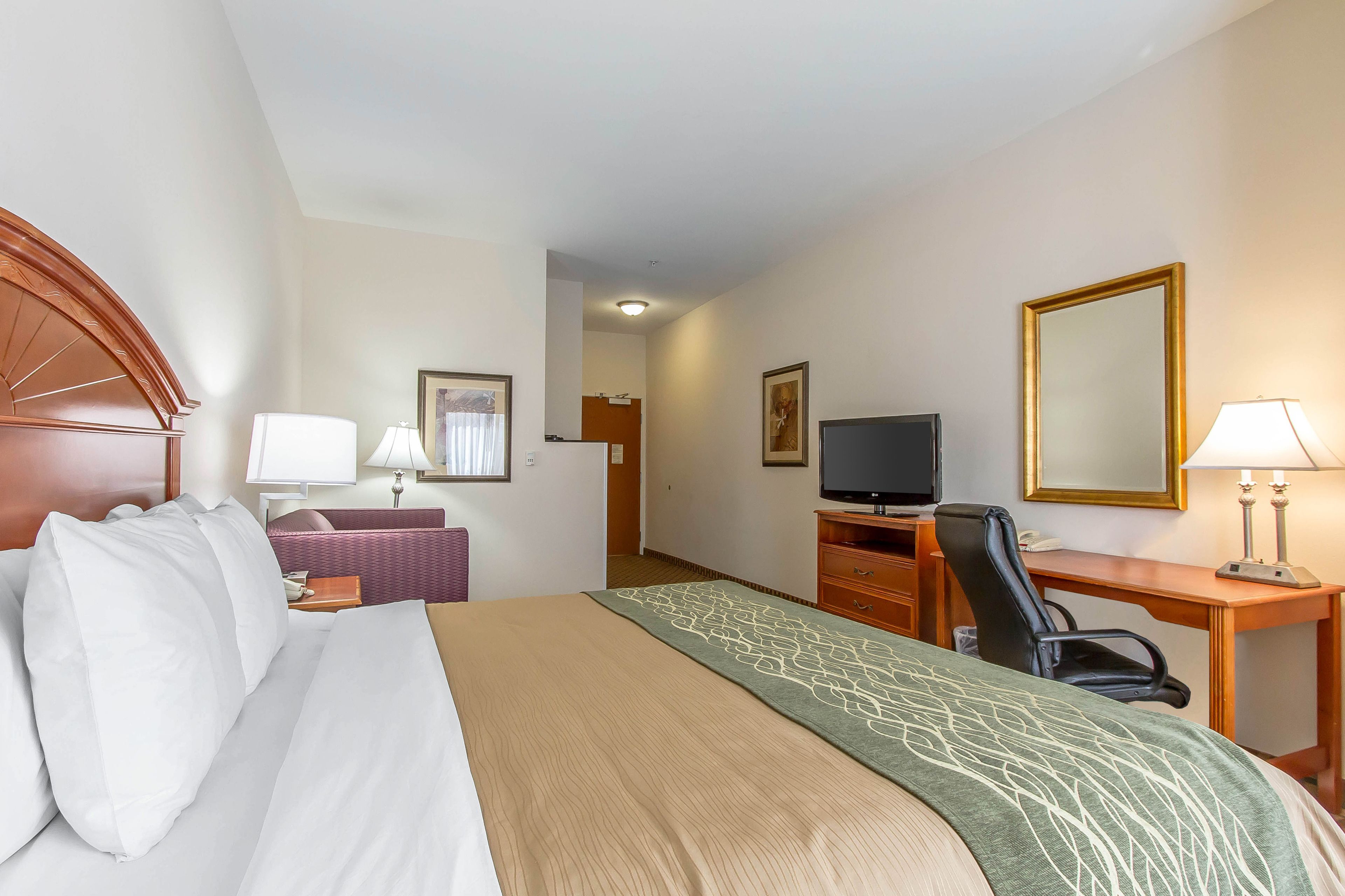 A hotel room with a bed, a desk, a chair, a television, and a mirror.