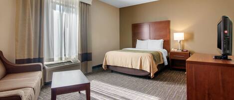 A hotel room with a bed, a desk, a chair, and a television.