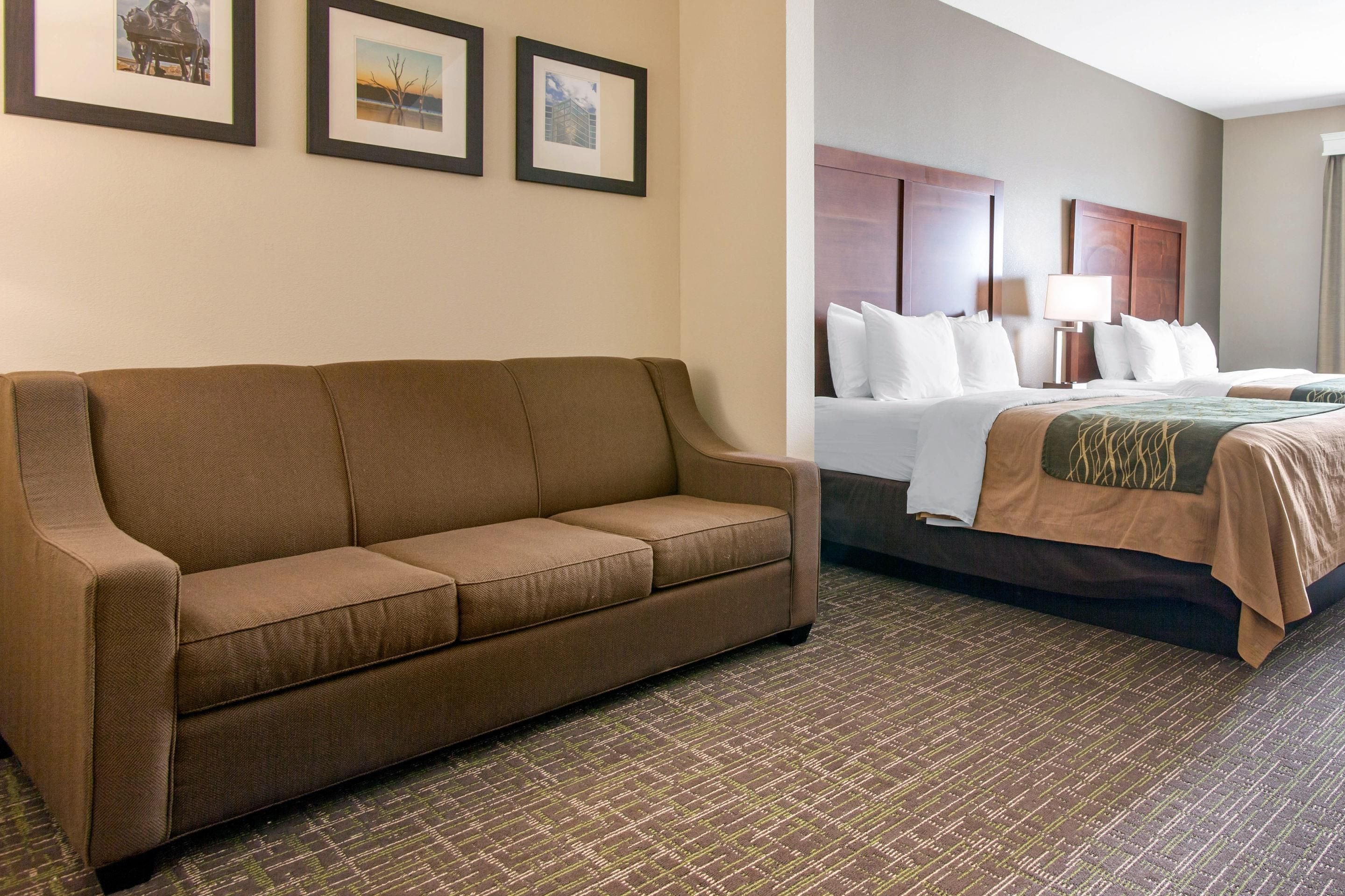 A hotel room with a brown sofa, a bed with a brown bedspread, and a patterned carpet.