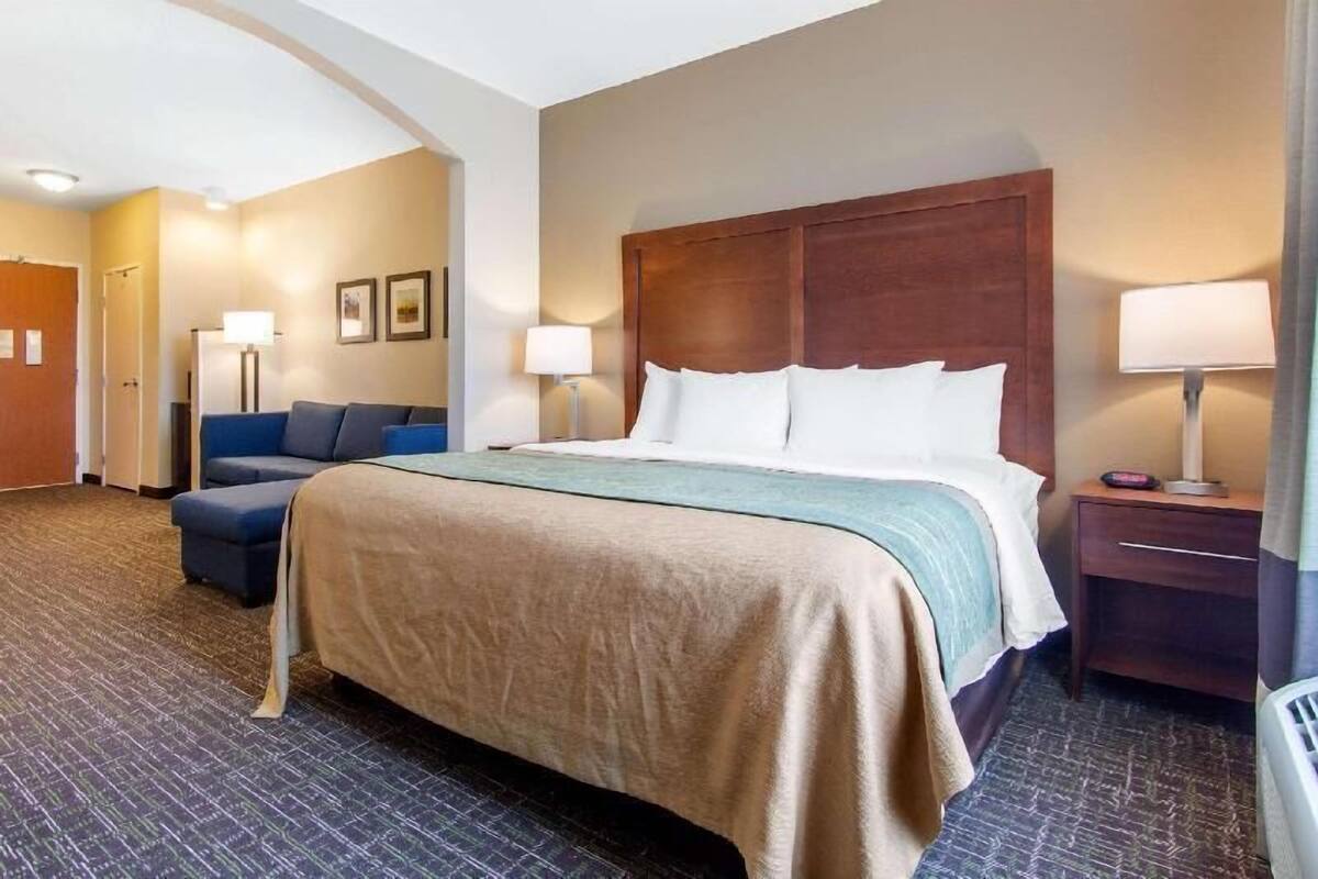 Una camera d'albergo con un letto, un divano, un comodino, una lampada e una porta.