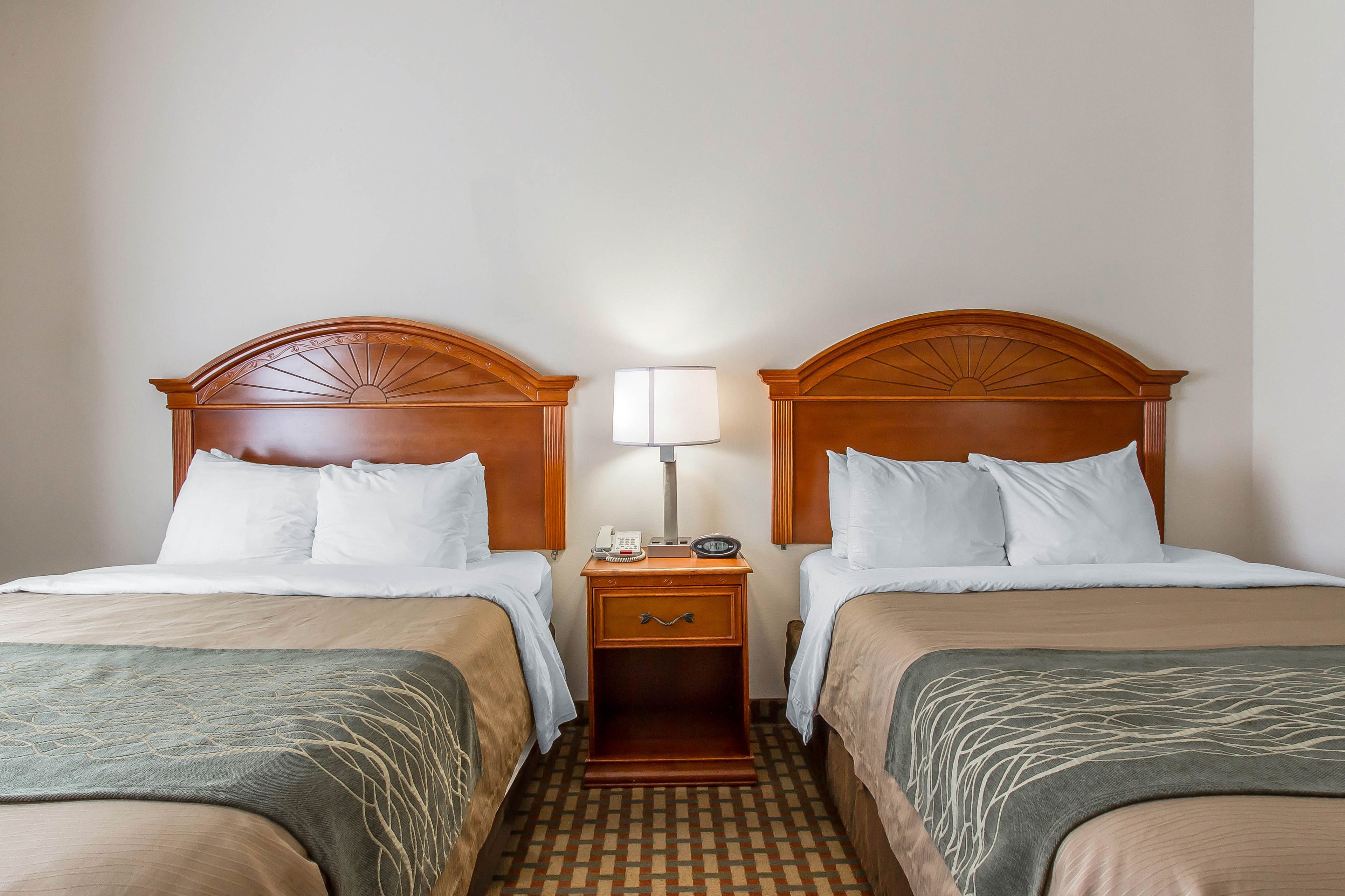 Habitación de hotel con dos camas, una mesita de noche con lámpara y un mostrador de recepción.
