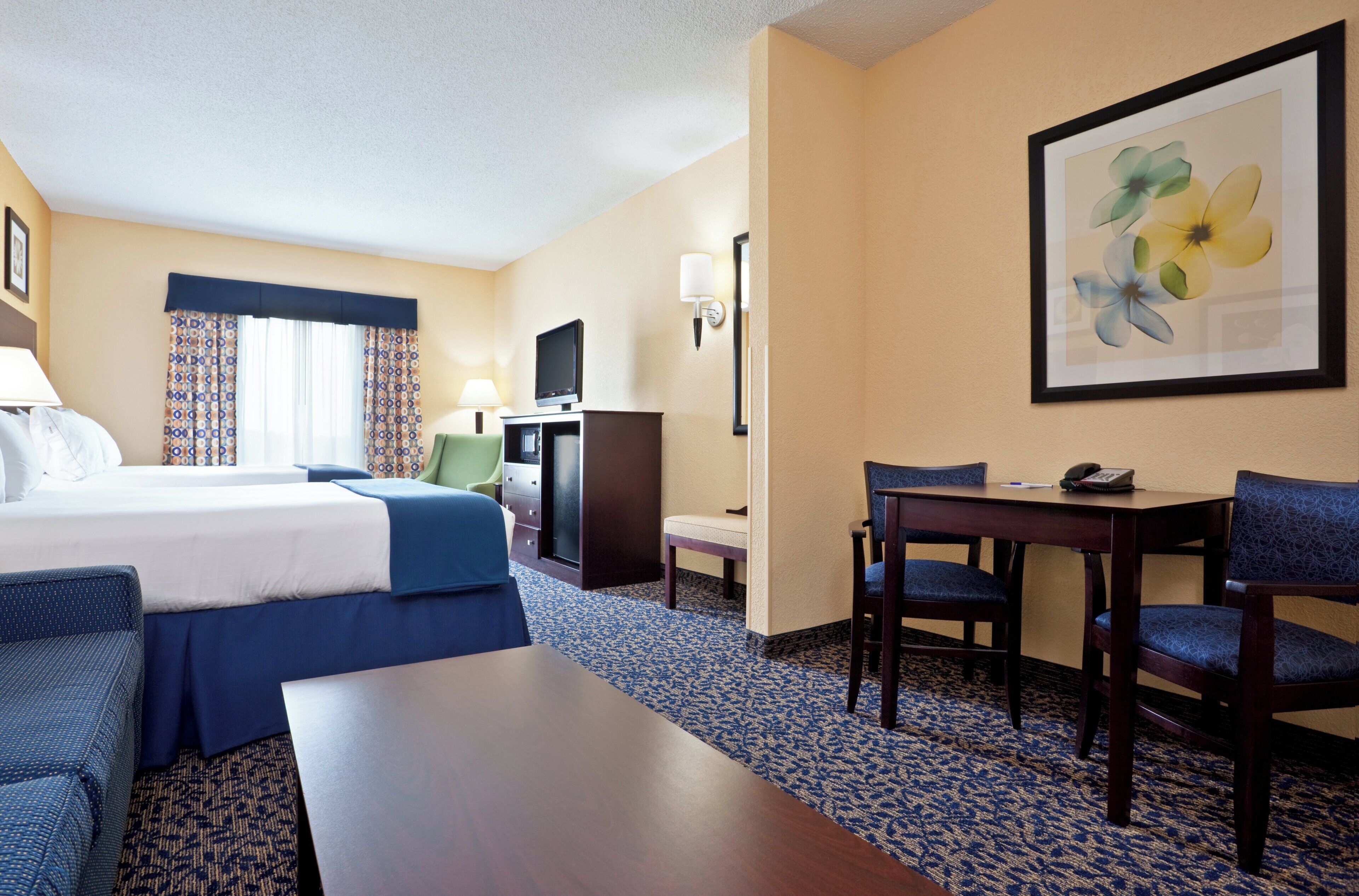 A hotel room with a bed, a desk, a chair, a television, and a painting on the wall.