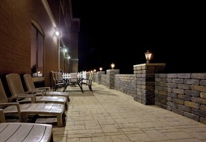 An outdoor patio area with tables and chairs, a brick wall, and decorative lighting. - Holiday Inn Express & Suites Akron Regional Airport Area by IHG (Akron)