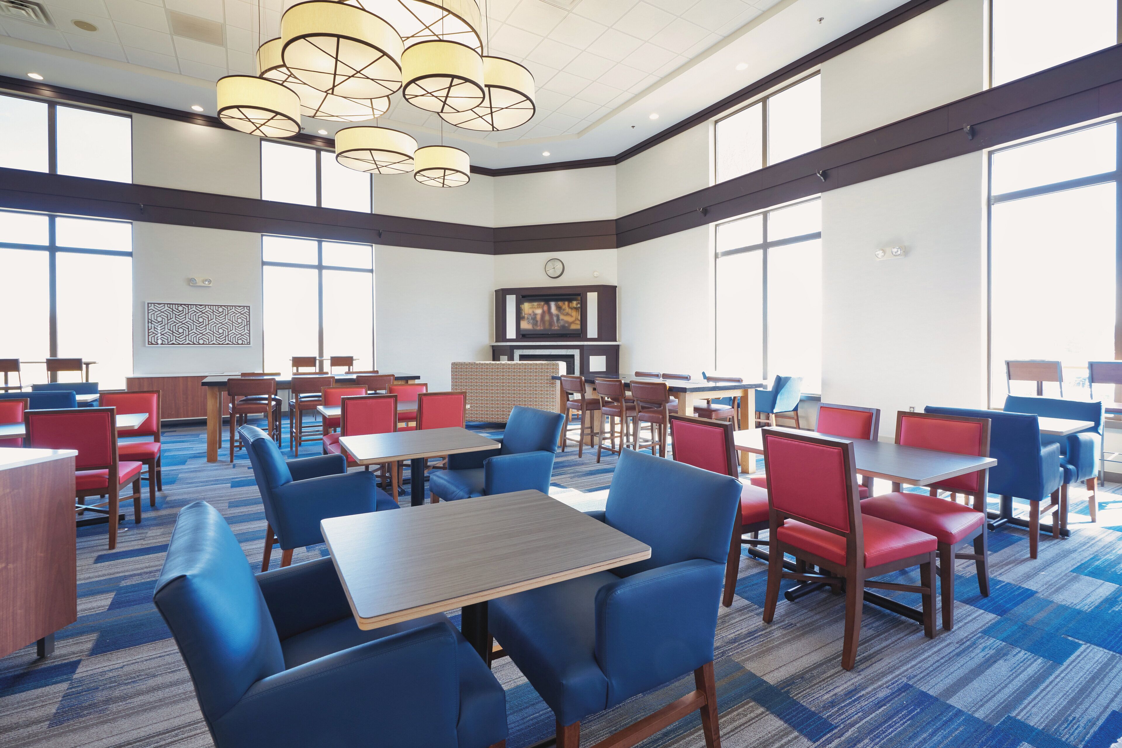 Un vaste espace dédié à la salle à manger, avec de nombreuses tables et chaises, de grandes fenêtres et un lustre moderne.