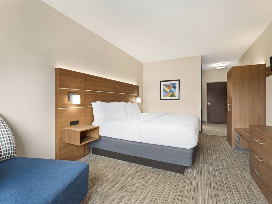 A hotel room with a bed, bedside table, lamp, wardrobe, and a television.