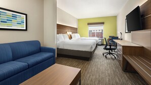 A hotel room with a blue sofa, two beds, a desk, and a television. - Holiday Inn Express & Suites Akron Regional Airport Area by IHG (Akron)