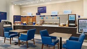 A breakfast area with a counter displaying various food options, a coffee machine, and seating with blue chairs and tables. - Holiday Inn Express & Suites Akron Regional Airport Area by IHG (Akron)