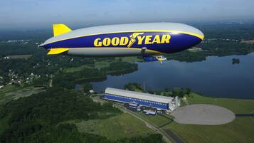 A Goodyear blimp flying over a rural area with a large building below.
