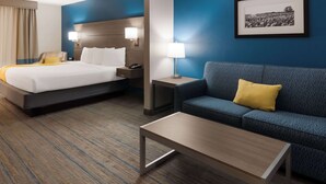 A hotel room with a bed, a sofa, a coffee table, a nightstand, a lamp, and a framed picture on the wall.