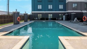A swimming pool with a tiled edge, lounge chairs, and a lifebuoy on a fence.