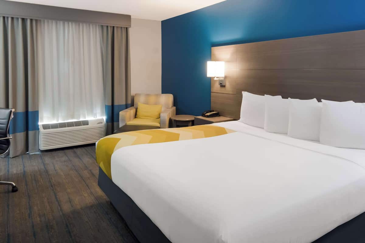 Ein Hotelzimmer mit einem großen Bett, einem Sessel, einem Schreibtisch und einem Nachttisch.