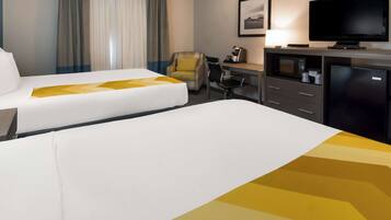 A hotel room with two beds, a desk with a computer, a television, and a refrigerator.