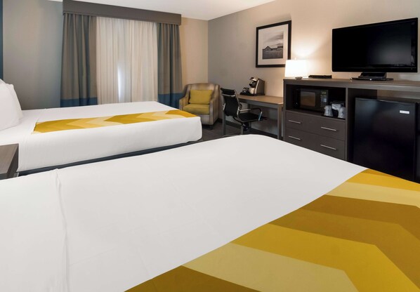 Una habitación de hotel con dos camas, un escritorio con computadora, televisión y refrigerador.