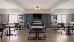 A spacious dining area with multiple tables and chairs, a flat-screen TV mounted on the wall, and a modern chandelier.