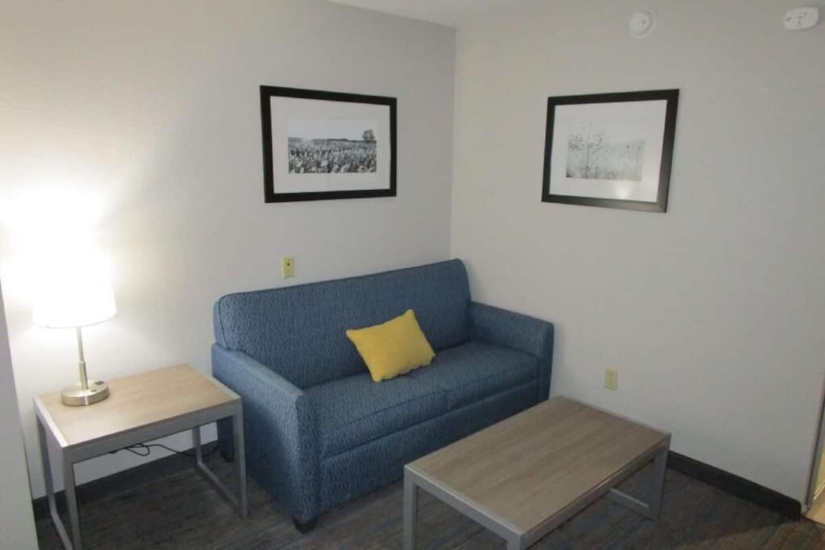 Ein Zimmer mit einem blauen Sofa, einem kleinen Tisch, zwei gerahmten Bildern an der Wand und einer Lampe auf einem Beistelltisch.