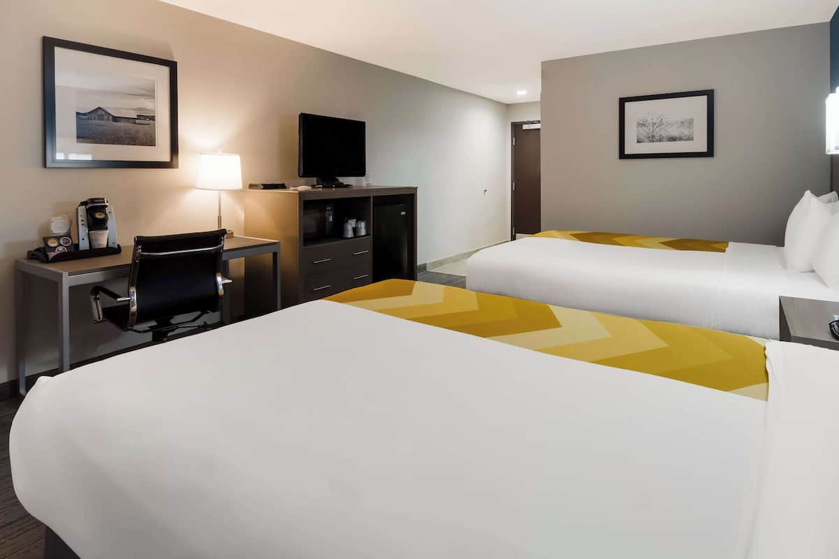 Ein Hotelzimmer mit zwei Betten, einem Schreibtisch mit Stuhl, einem Fernseher und einer Kaffeemaschine.