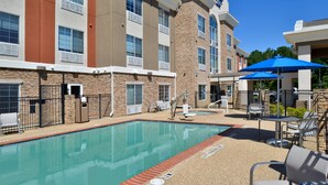A hotel with a swimming pool, outdoor seating, and a brick facade.