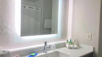 Et badeværelse med et stort spejl, en vask og toiletartikler på bordet.