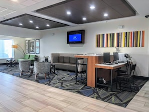 A modern office space with a sofa, chairs, a desk with computers, a television, and a colorful wall art piece.