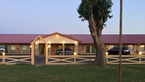 Un motel doté d’un parking couvert, d’un arbre et d’un bâtiment avec un toit rouge.