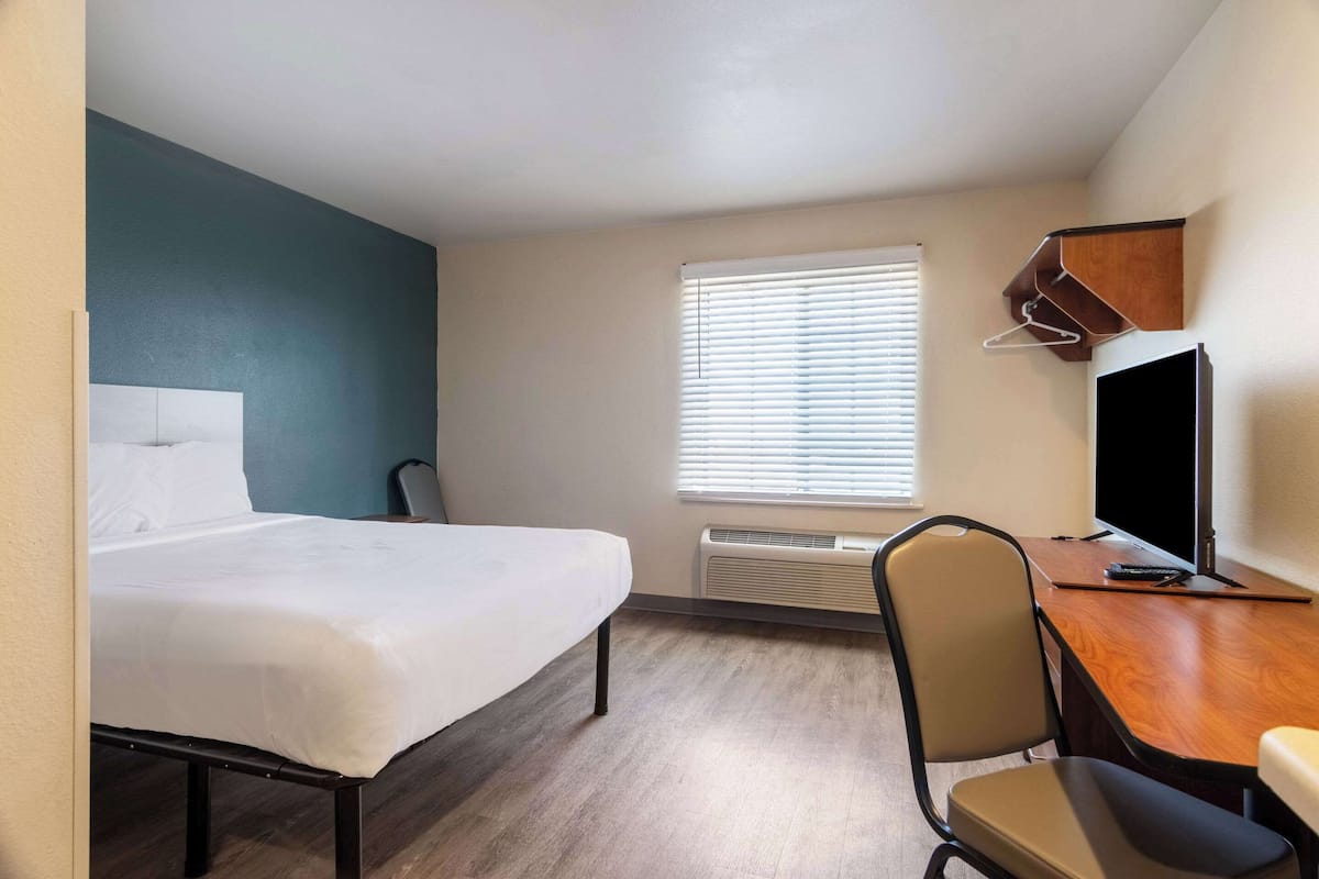 A hotel room with a bed, a desk, a chair, a TV, and a window with blinds.