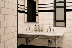A bathroom with a white tiled wall, a black-framed window, and a sink with two faucets. - West Village Eurohostel (New York)