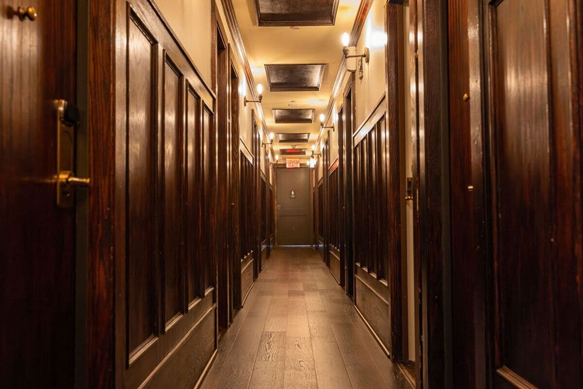 A long, narrow hallway with wooden doors on both sides, leading to a door at the end.