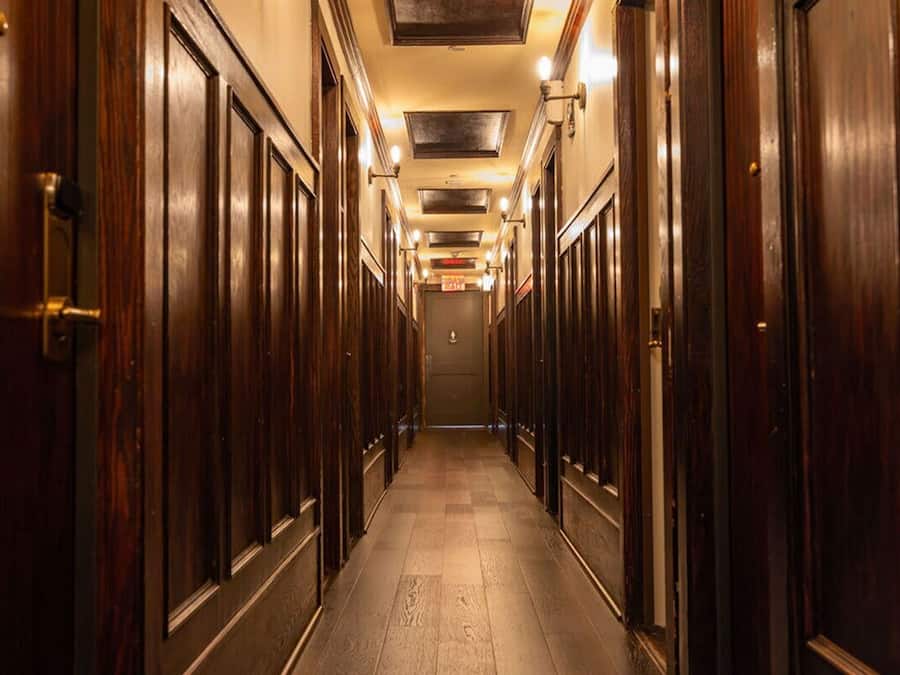 Un long couloir étroit, avec des portes en bois de chaque côté, qui mène à une porte au bout.