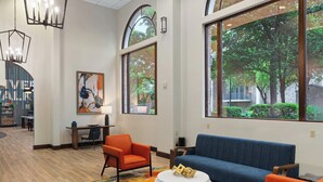 A modern lobby with a blue sofa, orange chairs, a round white coffee table, and large windows offering a view of trees. - Club Wyndham La Cascada (San Antonio)