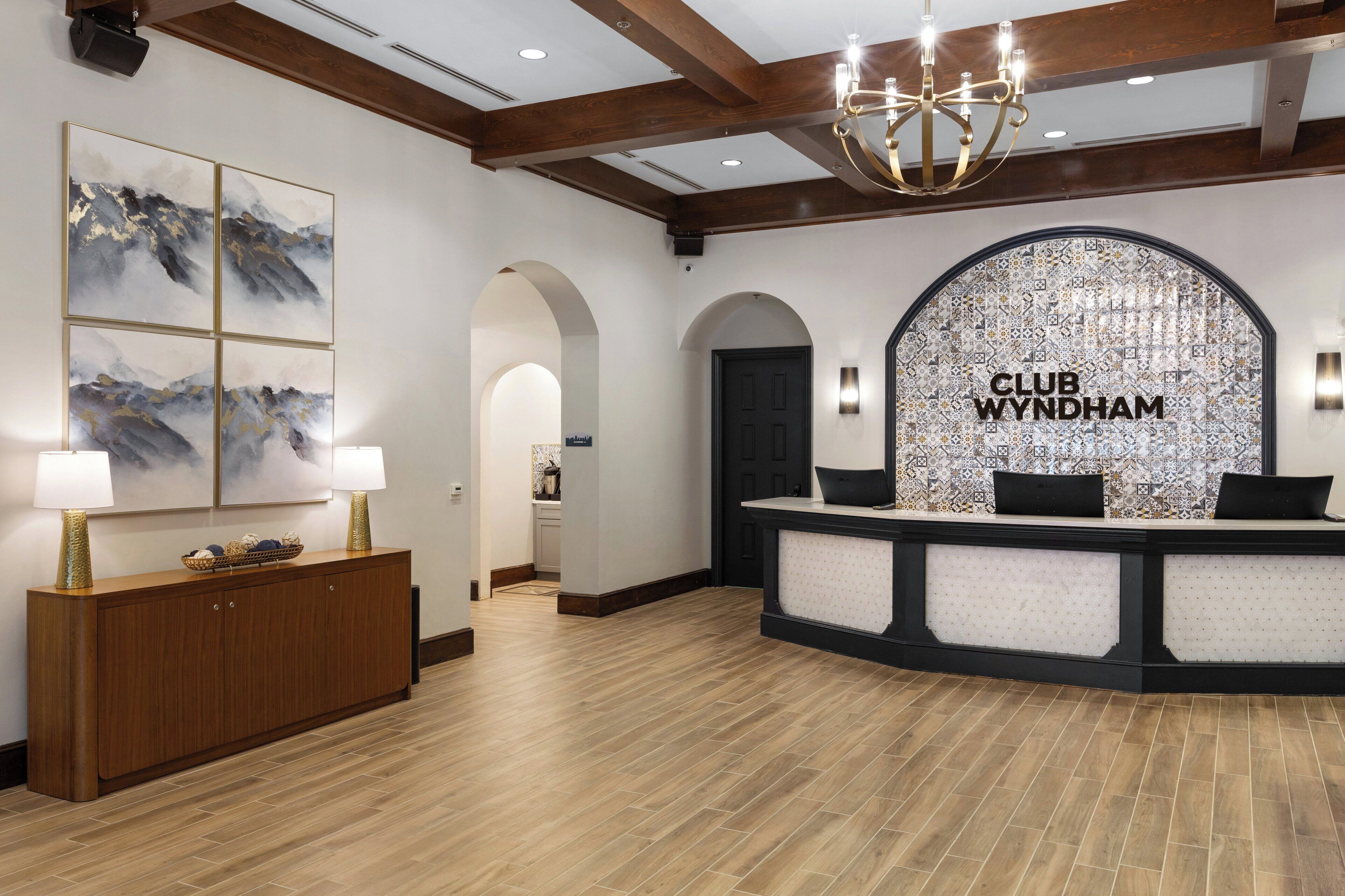 A reception area with a wooden reception desk, a chandelier, and a wall with 'CLUB WYNDHAM' signage.