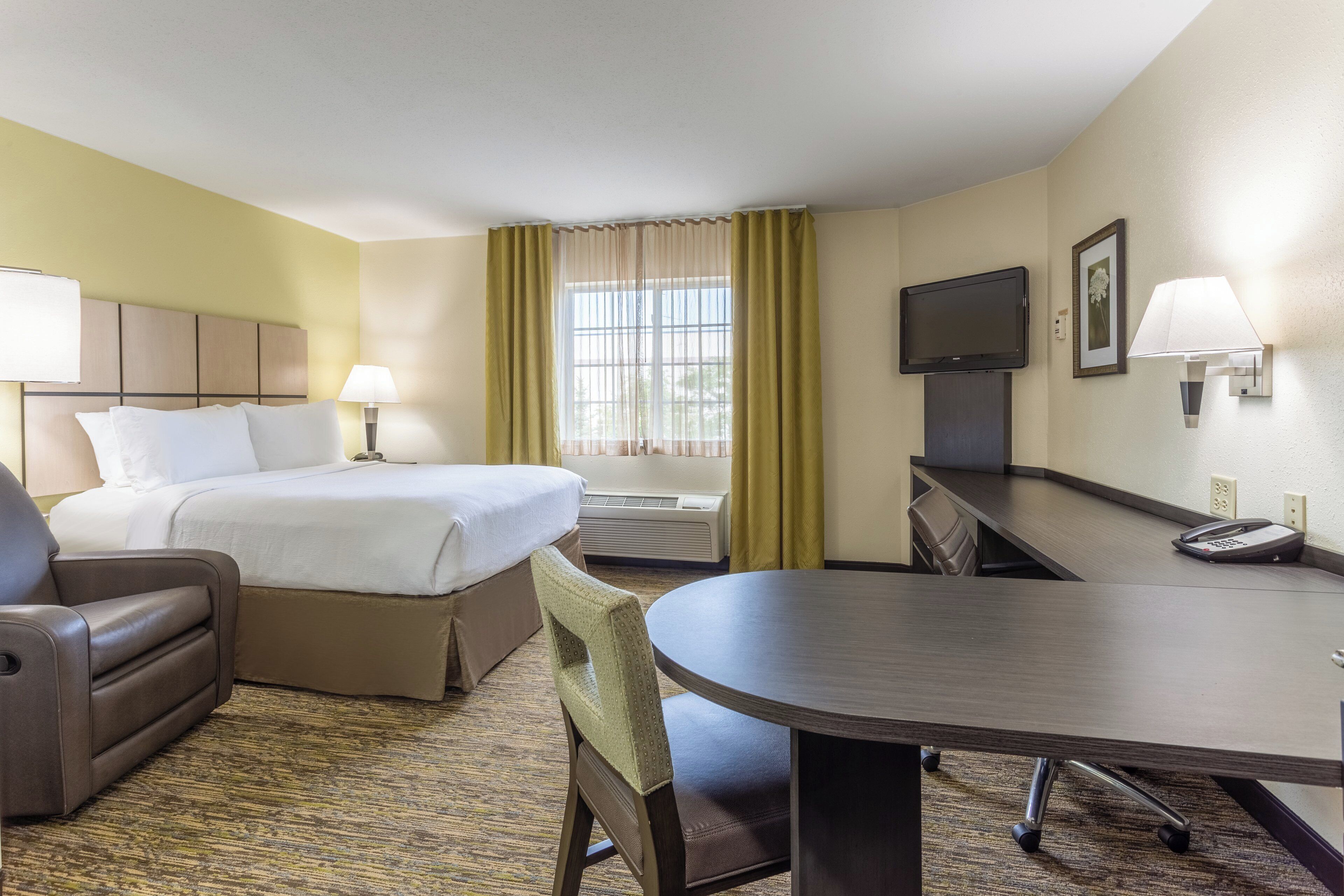 A hotel room with a bed, a desk, a chair, a TV, and a telephone.