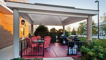 Un patio exterior con zona de estar techada, una parrilla para barbacoa y un dispensador de agua.