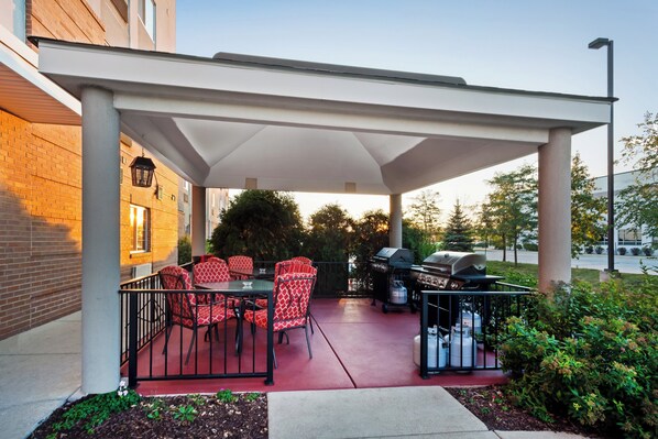 Un patio exterior con zona de estar techada, una parrilla para barbacoa y un dispensador de agua.