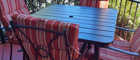 An outdoor patio with a metal table and striped cushioned chairs, surrounded by a metal railing and a view of a golf course.