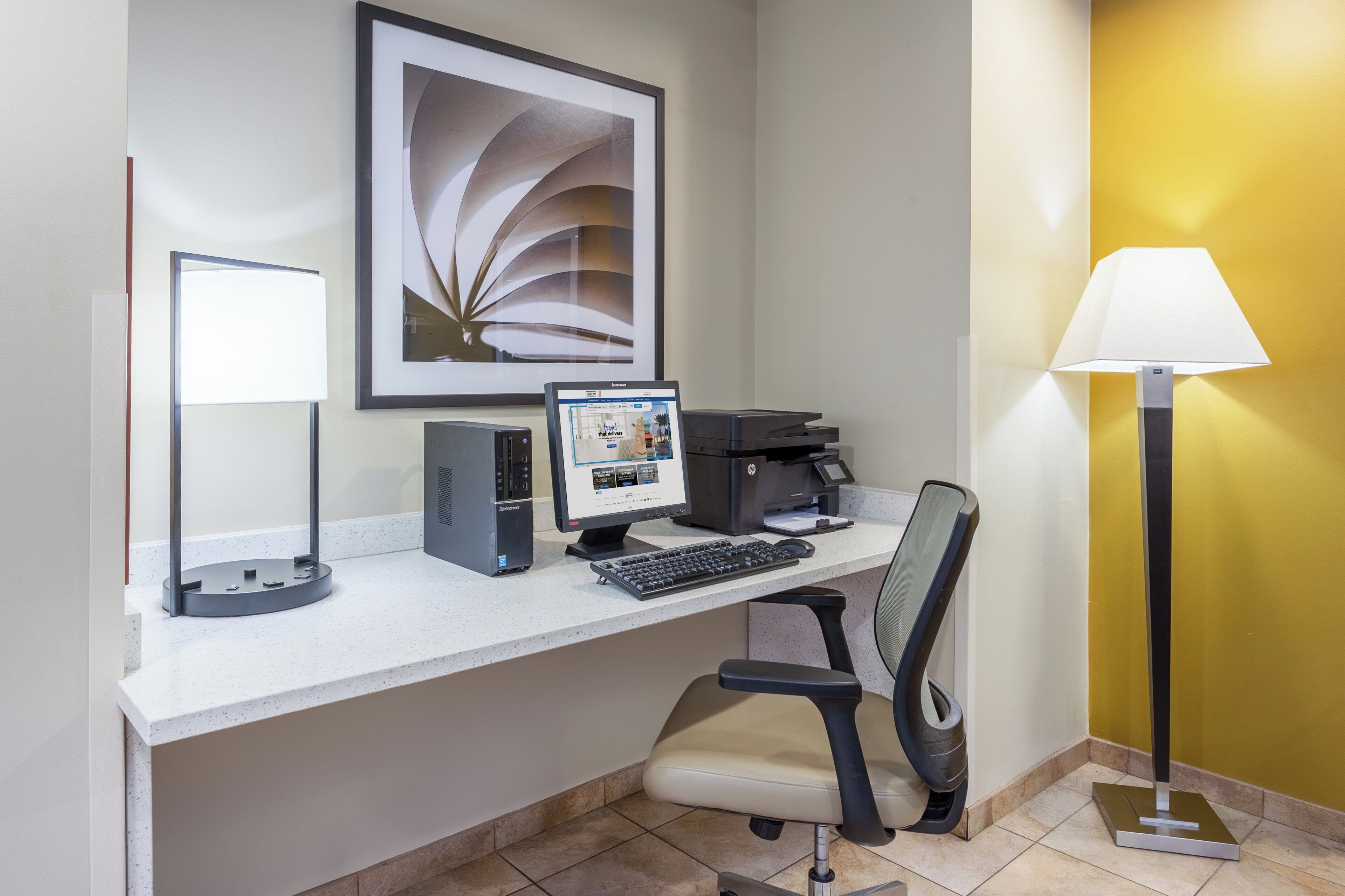 A hotel office desk with a computer, printer, and chair.