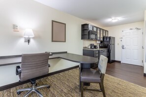 A compact hotel room with a kitchenette, a dining area with a table and chairs, a wall-mounted lamp, and a door. - Candlewood Suites Aurora-Naperville by IHG (Aurora)