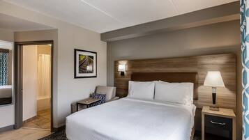 A hotel room with a large bed, bedside table, lamp, and a framed picture on the wall.