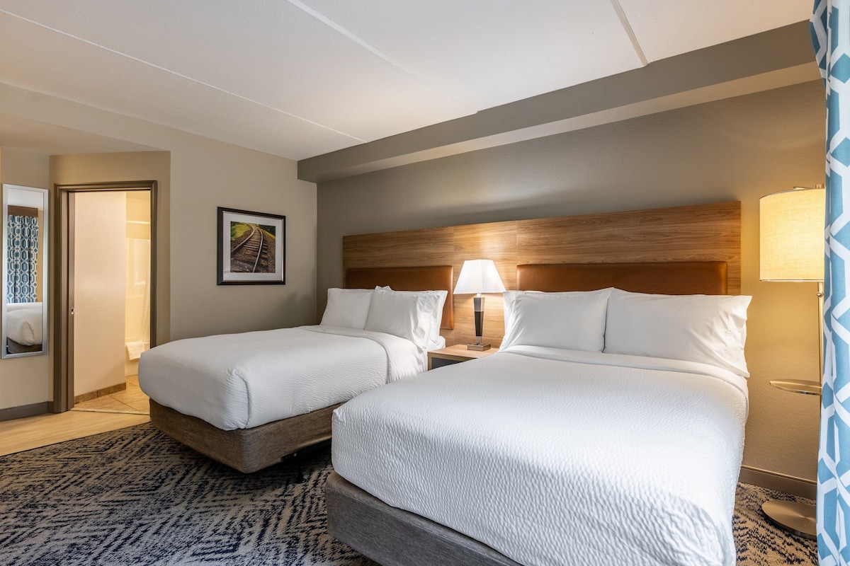 A hotel room with two beds, a wooden headboard, a framed picture on the wall, and a patterned rug.