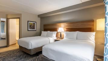 A hotel room with two beds, a headboard, a nightstand, a lamp, a framed picture, and a patterned rug.