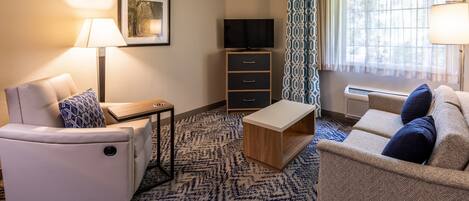 A hotel room with a sofa, a small table, a TV, a cabinet, and a window with curtains.