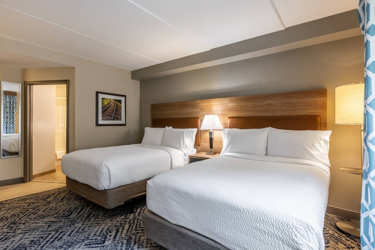 Une chambre d’hôtel avec deux lits, une tête de lit en bois, un tableau encadré au mur et un tapis à motifs.