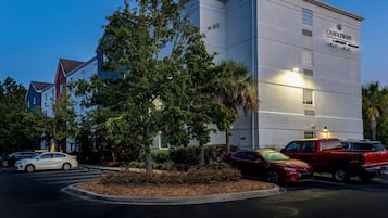 A hotel with a modern facade, a parking lot with several cars, and a landscaped area with red flowers.