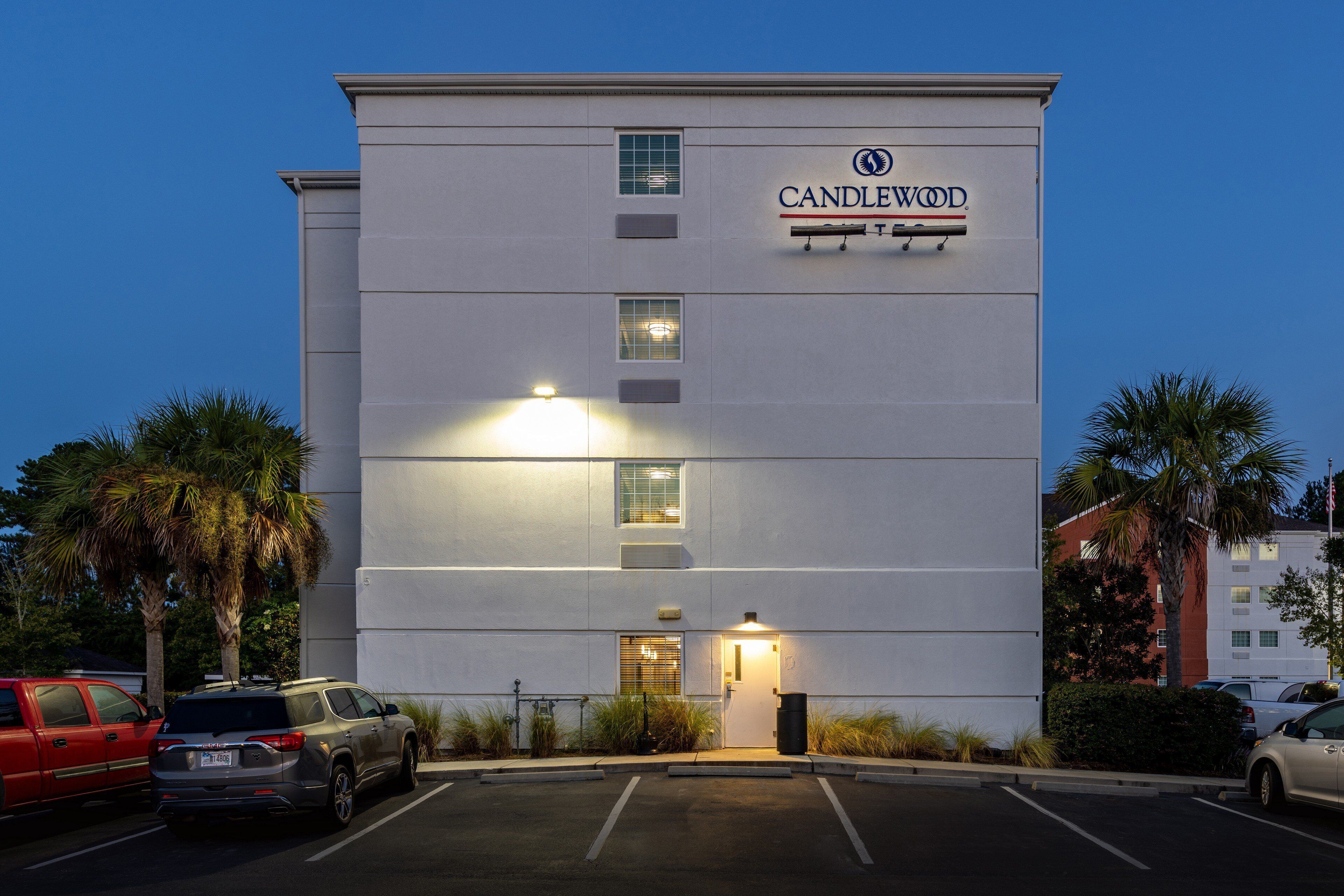 A multi-story hotel with a flat facade, a visible entrance, and a parking lot with several cars.