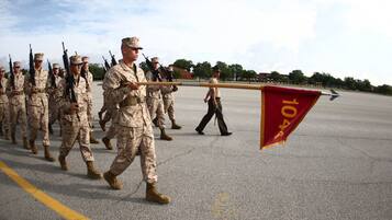 A group of military personnel in uniform marching on a paved surface with a flag being carried.