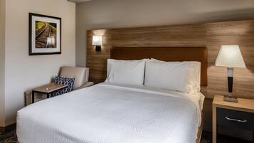 Habitación de hotel con una cama grande, una mesita de noche con lámpara, una silla y un cuadro en la pared.